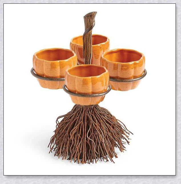 A Halloween-themed snack stand with a broom and three pumpkin-shaped bowls for serving treats and snacks