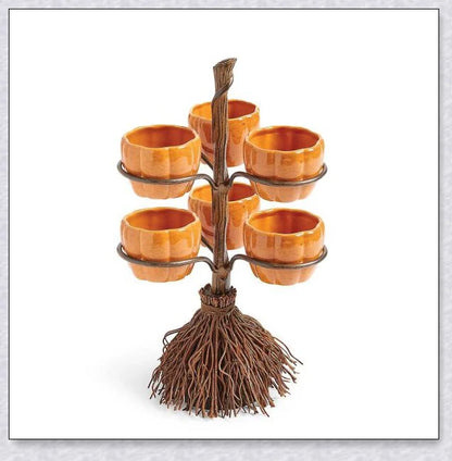 A Halloween-themed snack stand with a broom and three pumpkin-shaped bowls for serving treats and snacks