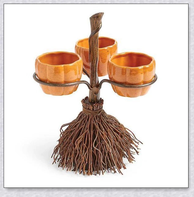 A Halloween-themed snack stand with a broom and three pumpkin-shaped bowls for serving treats and snacks