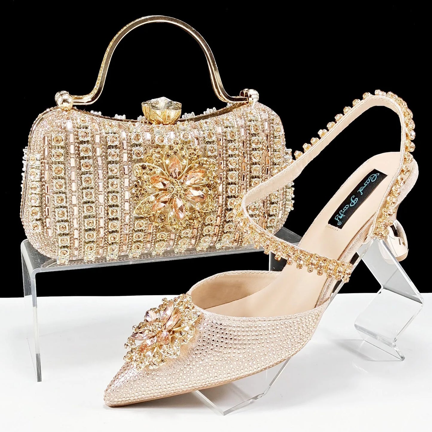 Women's black high-heel ankle strap shoes with floral rhinestone buckle and matching clutch bag on a neutral background