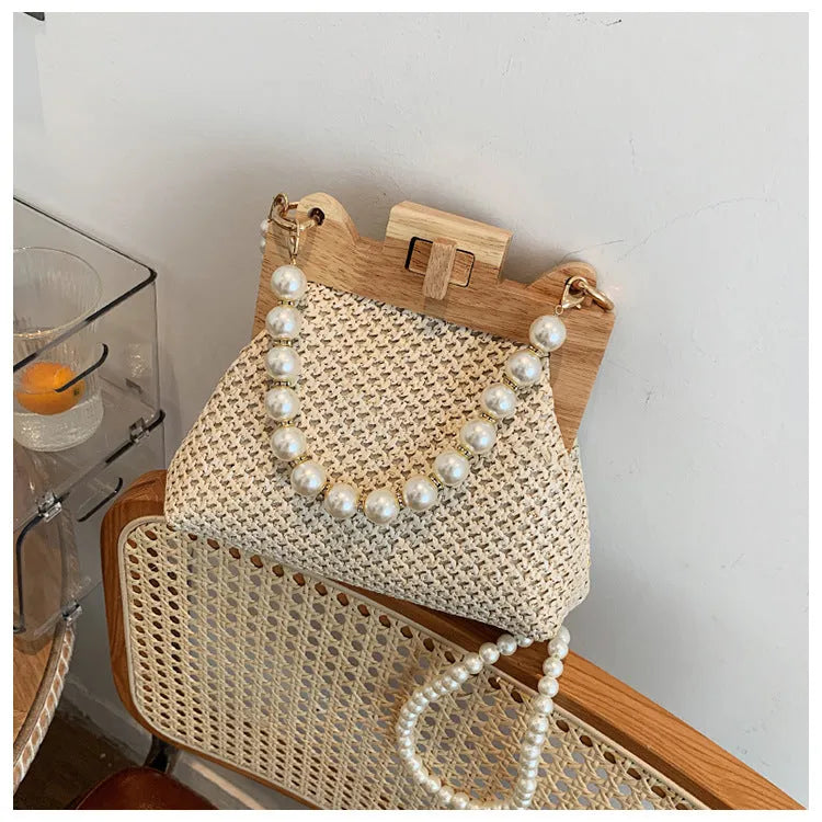 Women's beige straw woven shoulder bag with pearl chain strap, showing horizontal square shape and sewing line detail.