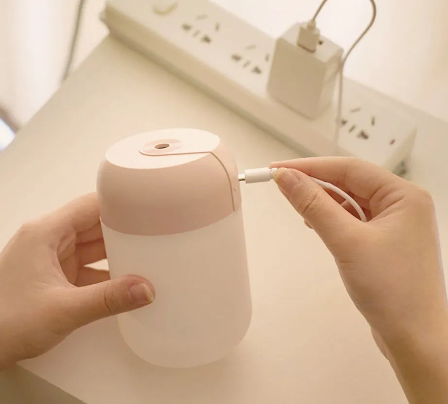 White cylindrical humidifier with USB cable on a desk, showing compact 15cm height and aromatherapy function for essential oils.