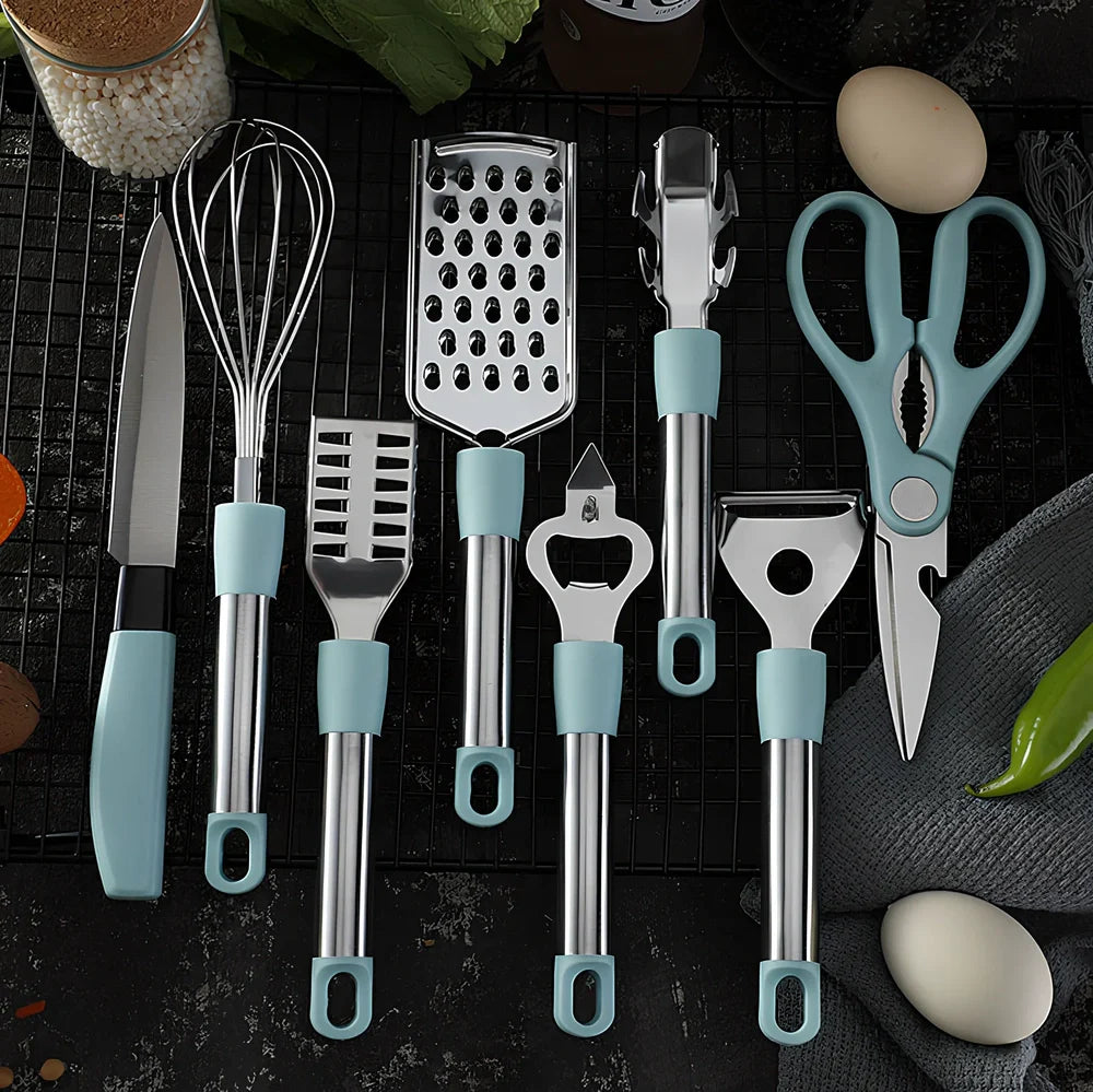 Stainless steel kitchen utensil set with whisk, grater, peeler, scissors and other tools on grey background