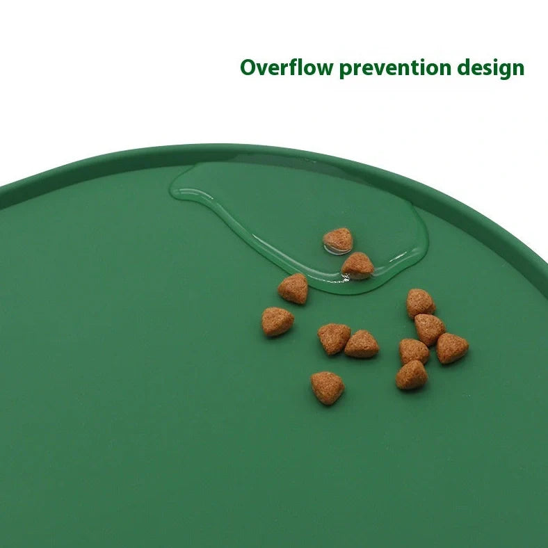 Green silicone cat feeding placemat with raised edges on wooden floor containing water bowl