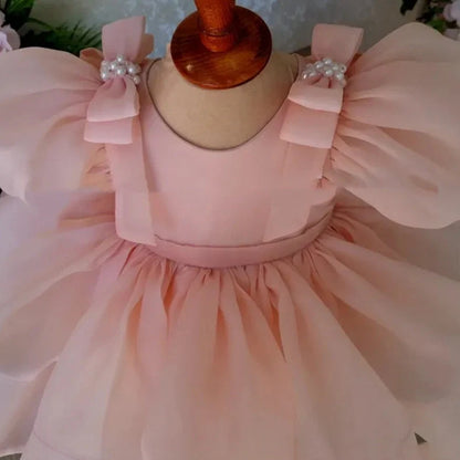 Pink flower girl dress with puffy sleeves and princess bow, shown on mannequin