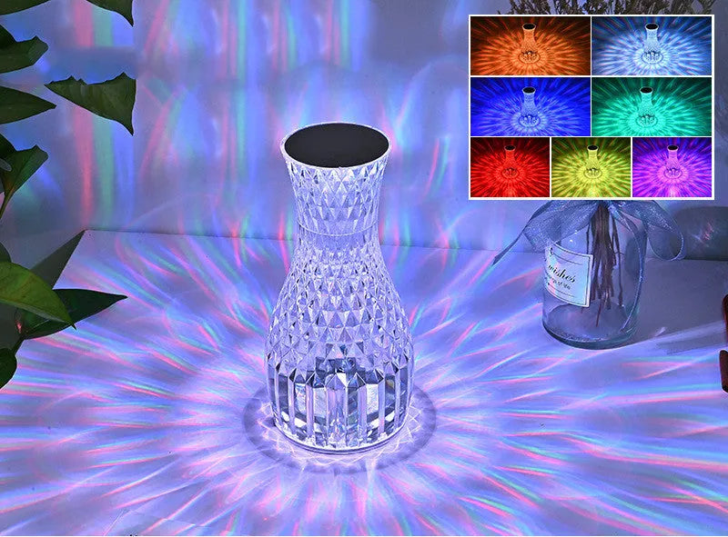Transparent vase-shaped crystal table lamp with remote control on a wooden bedside table.