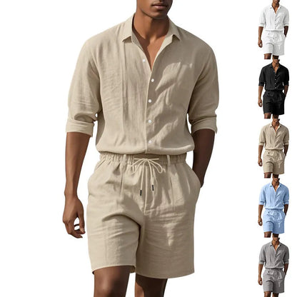 A man wearing a light blue linen long sleeve shirt and matching shorts on the beach.