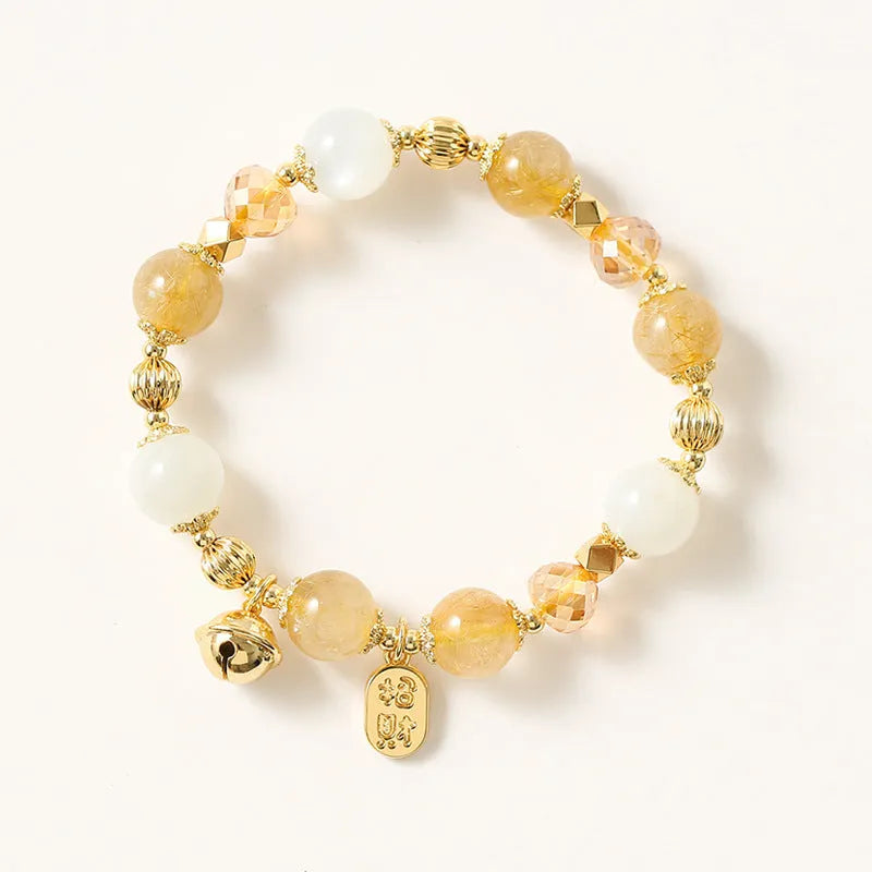 Gold-coloured rutilated quartz bracelet with a ringing bell charm on an adjustable band.