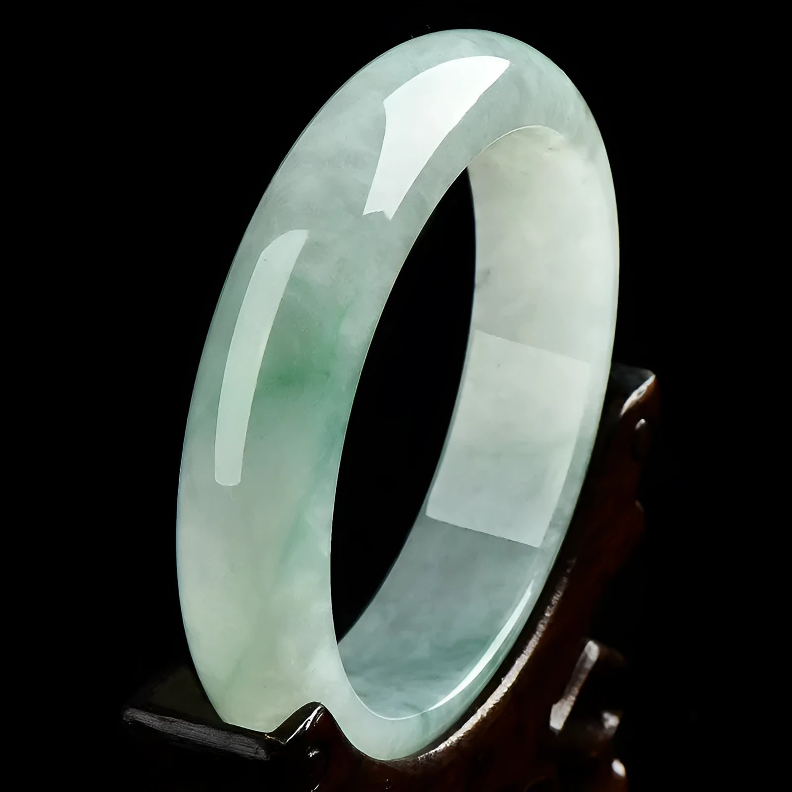 Light green solid jade bracelet on a wrist, showing its simple loop design and natural stone colour.