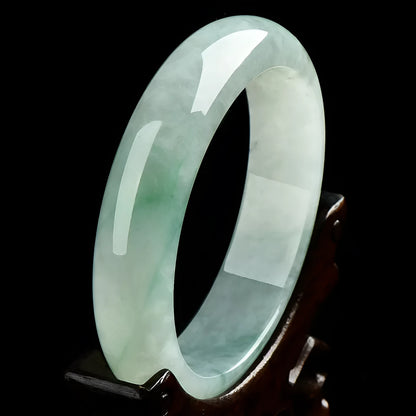 Light green solid jade bracelet on a wrist, showing its simple loop design and natural stone colour.