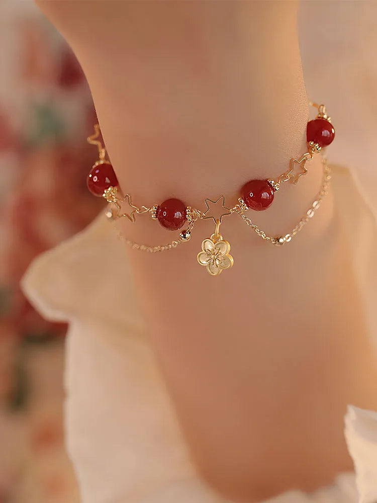 Red agate double layer bracelet with flower and peach blossom charms on a wrist.