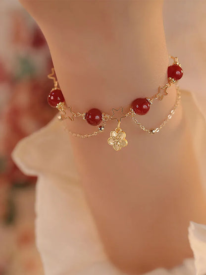 Red agate double layer bracelet with flower and peach blossom charms on a wrist.