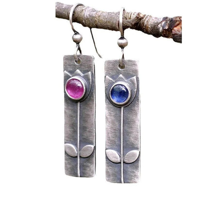 Geometric ellipse-shaped antique finish earrings with red sapphire stones on a white background.