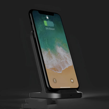 Dark grey vertical wireless charging stand for Apple iPhone on a desk.