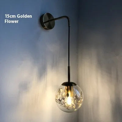 Glass wall lamp with golden flower finish and 15cm diameter, mounted beside bed with LED illumination