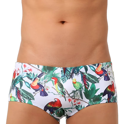Men's blue swimming trunks with a detailed floral and bird print pattern, shown in a brief style.