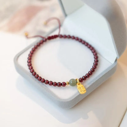 A hand-woven red rope bracelet with a strawberry quartz or garnet crystal, shown in simple styling.