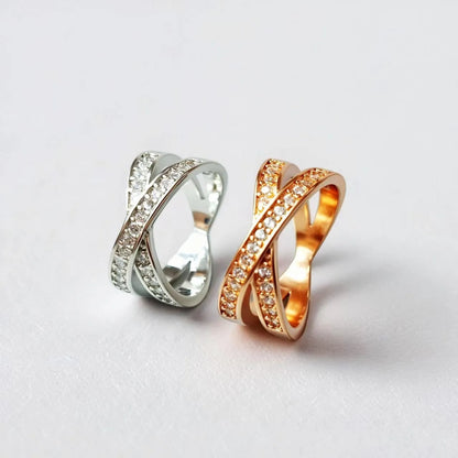 Silver geometric cross ring with micro-inlaid zircon stones on finger, showing simple design with heart-shaped elements