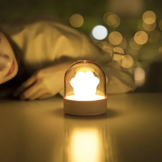 Grey cat paw shaped night light with USB port and button, glowing softly on a wooden desk.