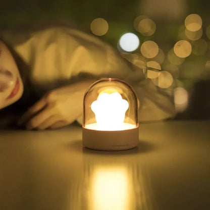 Grey cat paw shaped night light with USB port and button, glowing softly on a wooden desk.
