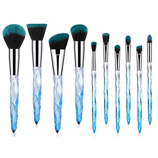 Ten clear crystal-handled foundation brushes with black synthetic bristles laid out on a surface.