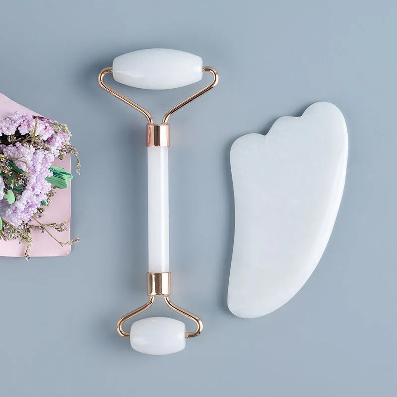 White jade facial roller with double heads and matching scraping board on dark surface