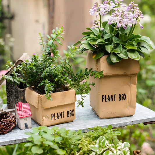 Square cement planter with matte finish and drainage holes, next to a small green plant.