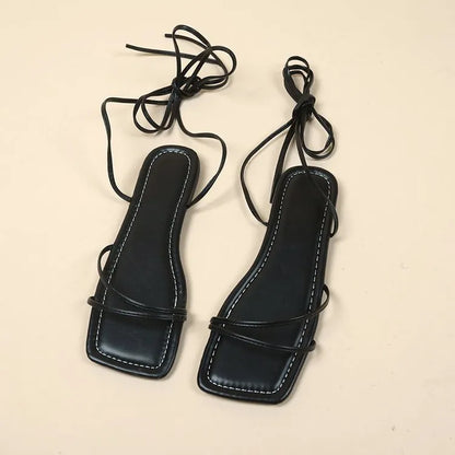 Women's black flat sandals with bandage ankle wrap and front lace-up fastening on a white background.