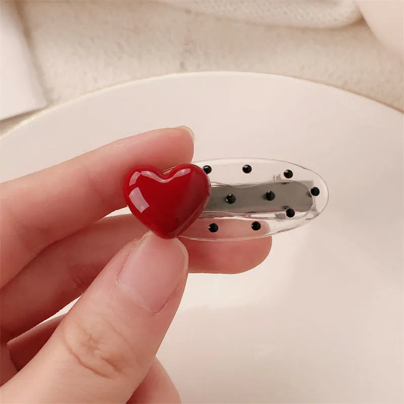 Red plastic hair clip with a 3D love heart and dots on a willow leaf-shaped base.