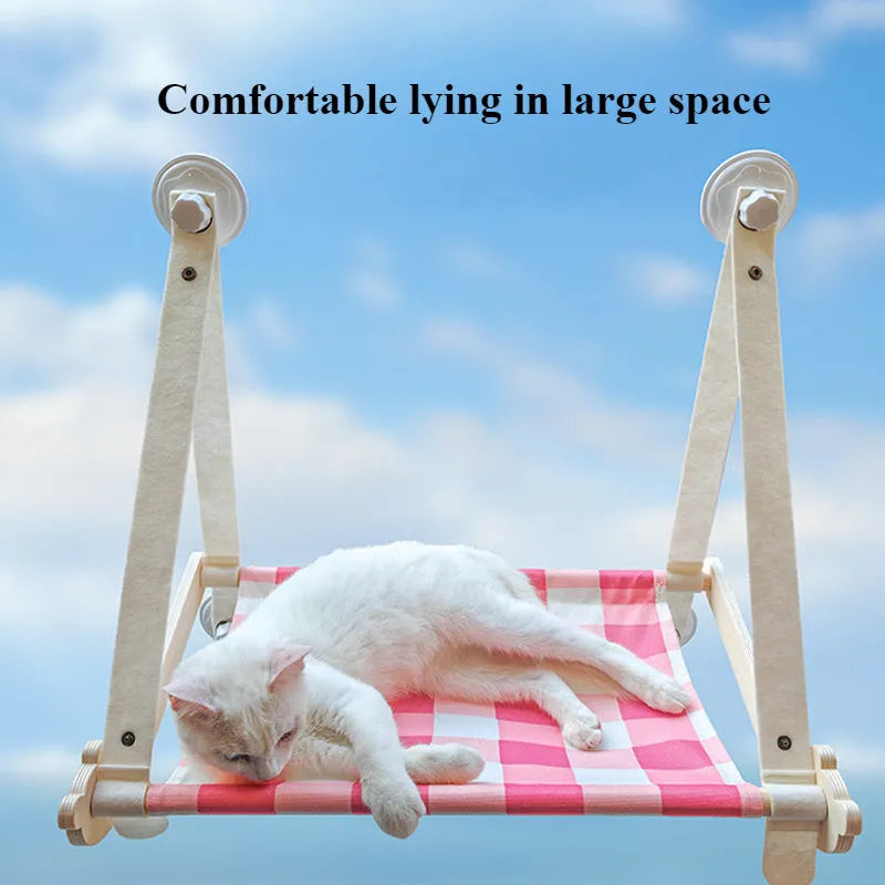 Pink cat hammock with wooden frame and suction cups attached to a window, with a cat resting inside.