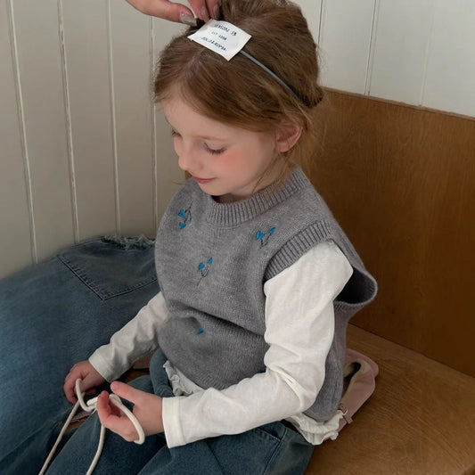 Light grey knitted vest with embroidered details for girls, shown on hanger