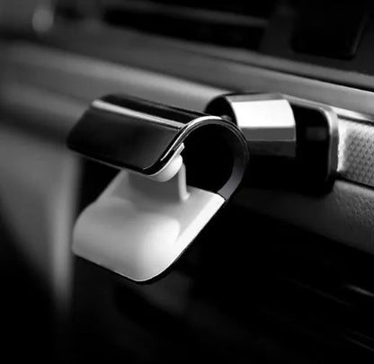 Black universal car phone holder with 360-degree rotating head mounted on a car air vent, holding a mobile phone.