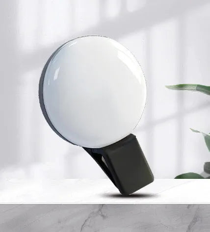Round black mobile phone fill light with adjustable clip attached to a smartphone.