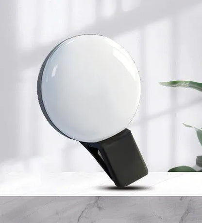 Round black mobile phone fill light with adjustable clip attached to a smartphone.