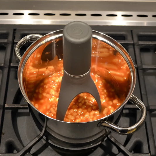 Uutensil Stirr automatic electric kitchen mixer device in green, shown next to a saucepan.