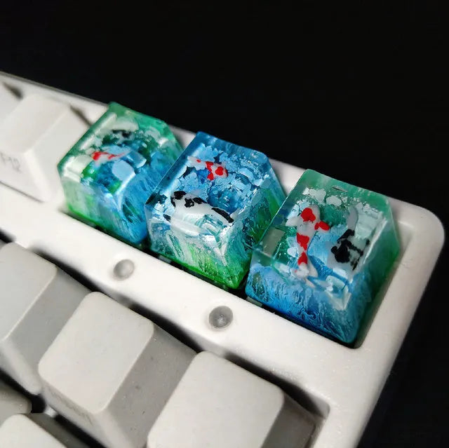Close-up of a custom resin keycap featuring a detailed blue and orange koi fish scene, designed for Cherry MX mechanical keyboards.