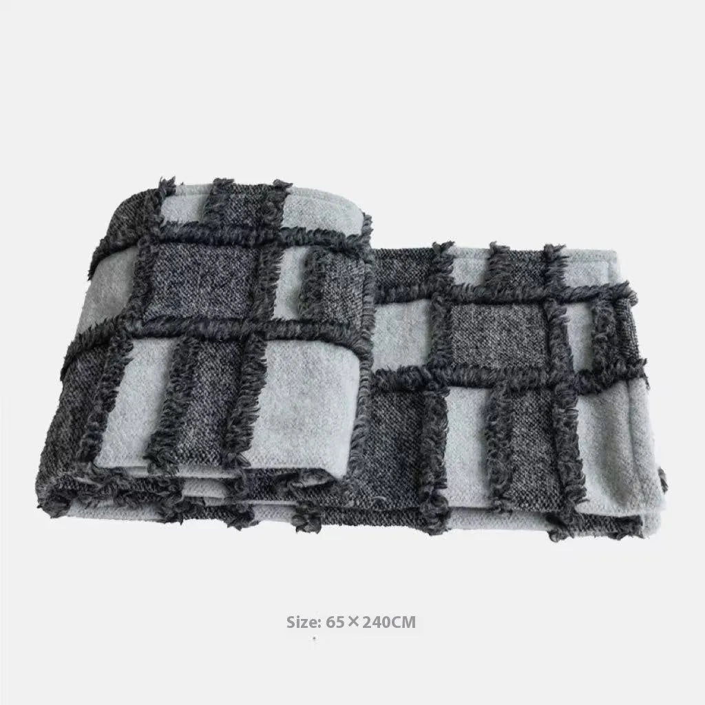 Grey and white plaid bed runner blanket with coordinating pillowcase and round leather pillow on bed