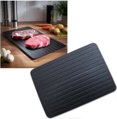 Black aluminium fast defrosting tray for kitchen use, shown thawing frozen meat.