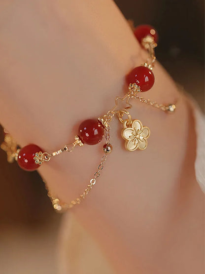Red agate double layer bracelet with flower and peach blossom charms on a wrist.