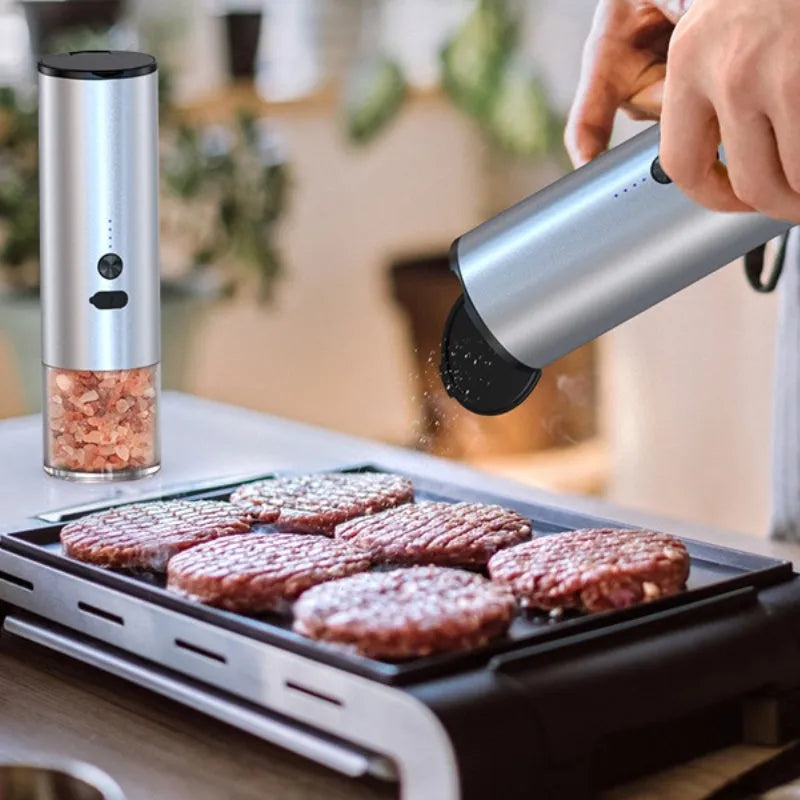 White electric salt and pepper grinder with stainless steel top and clear glass jar on a kitchen counter.