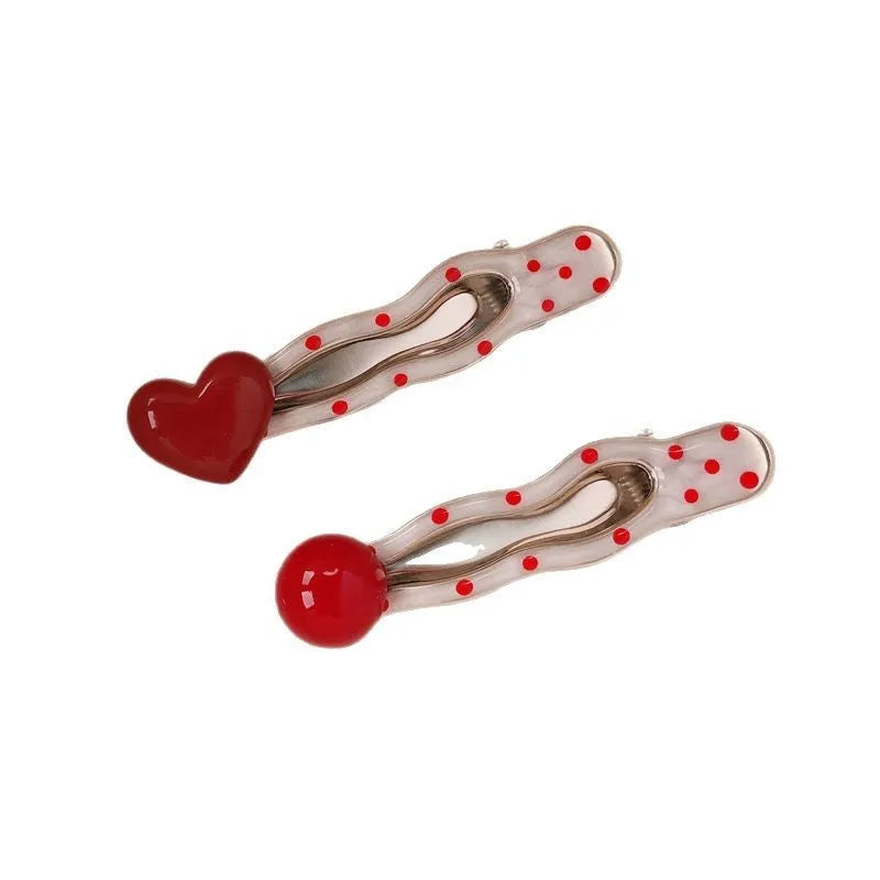 Red plastic hair clip with a 3D love heart and dots on a willow leaf-shaped base.