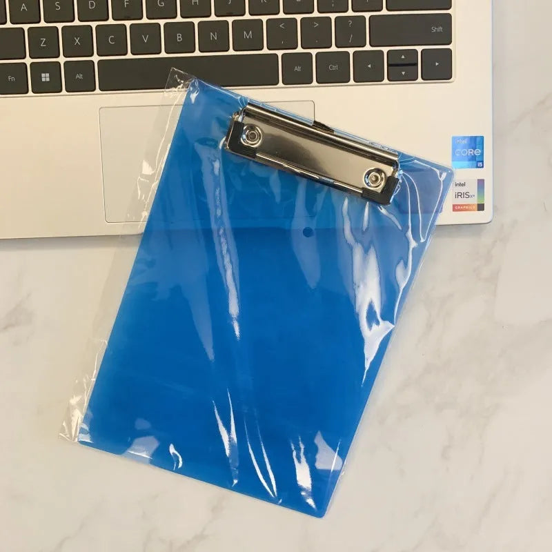 Transparent A4 writing board pad with metal flat clip in blue, alongside A5 size in red on a desk.