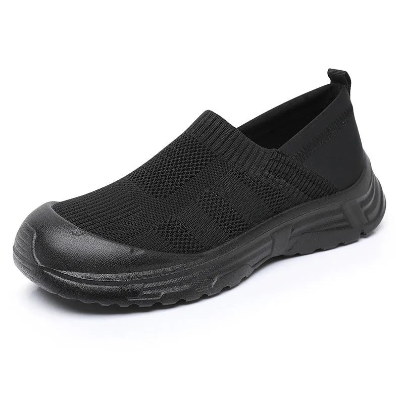 Women's one pedal slip-on shoe in black with cloth upper and PVC sole, showing round toe and flat heel design.