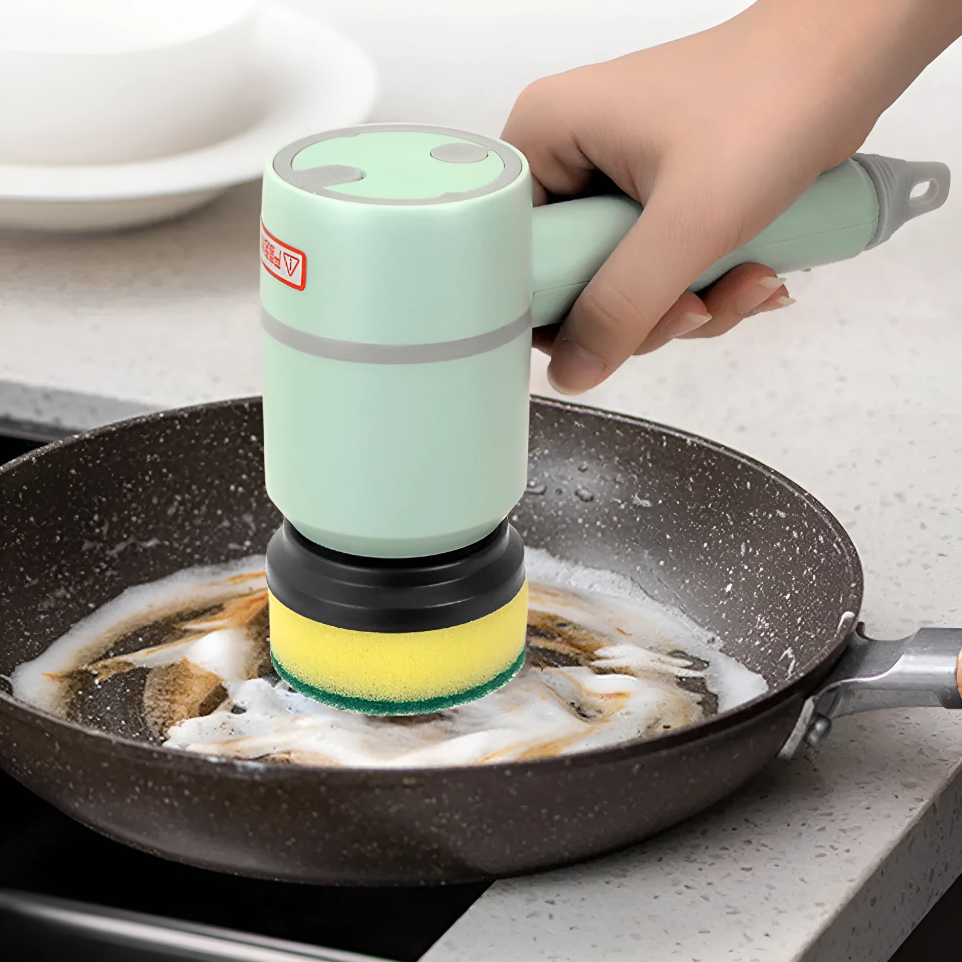 Green electric cleaning brush with scouring pad and brush heads on a kitchen worktop.