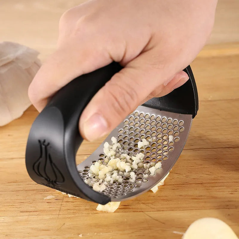 Stainless steel garlic press with coloured handles in a modern design, shown on a kitchen counter.