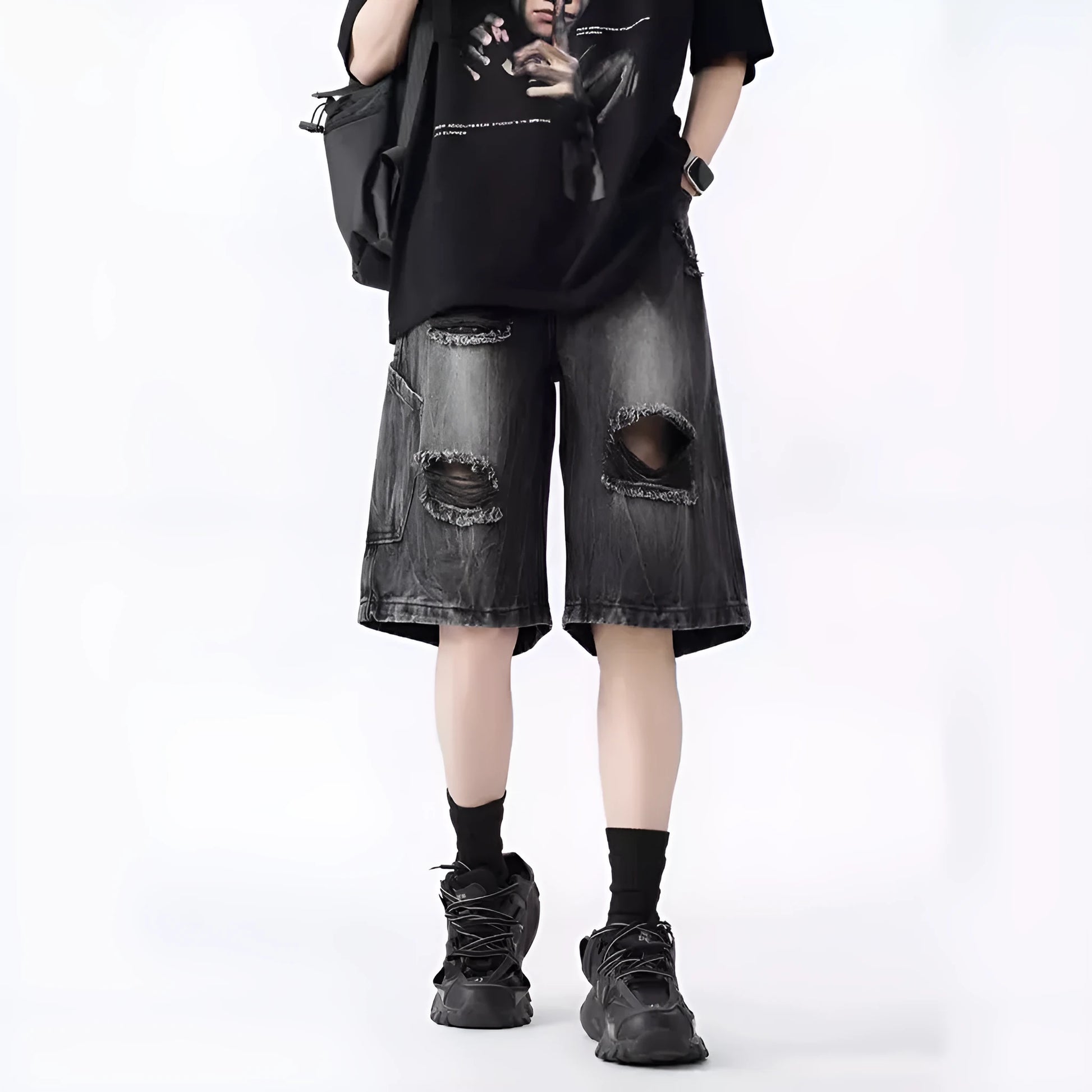 Man wearing loose fit black ripped denim shorts with distressed detailing and a washed vintage finish.