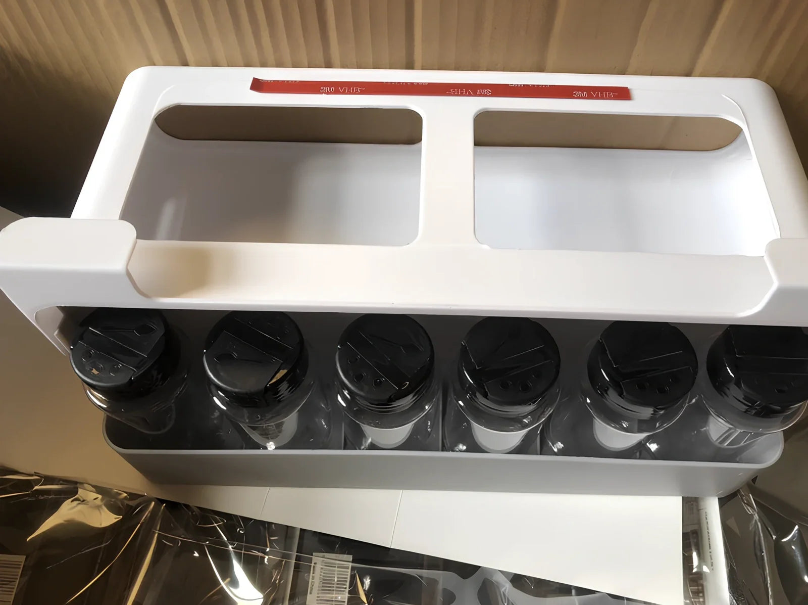 White plastic hanging spice rack with six clear glass bottles, mounted on kitchen door for punch-free storage