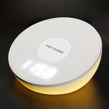 White wireless charging stand with digital clock display, showing time, next to a mobile phone on its angled charging platform.