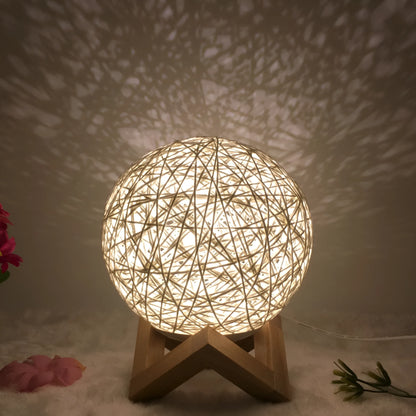 Spherical hand-knitted rattan table lamp with remote control on a wooden desk