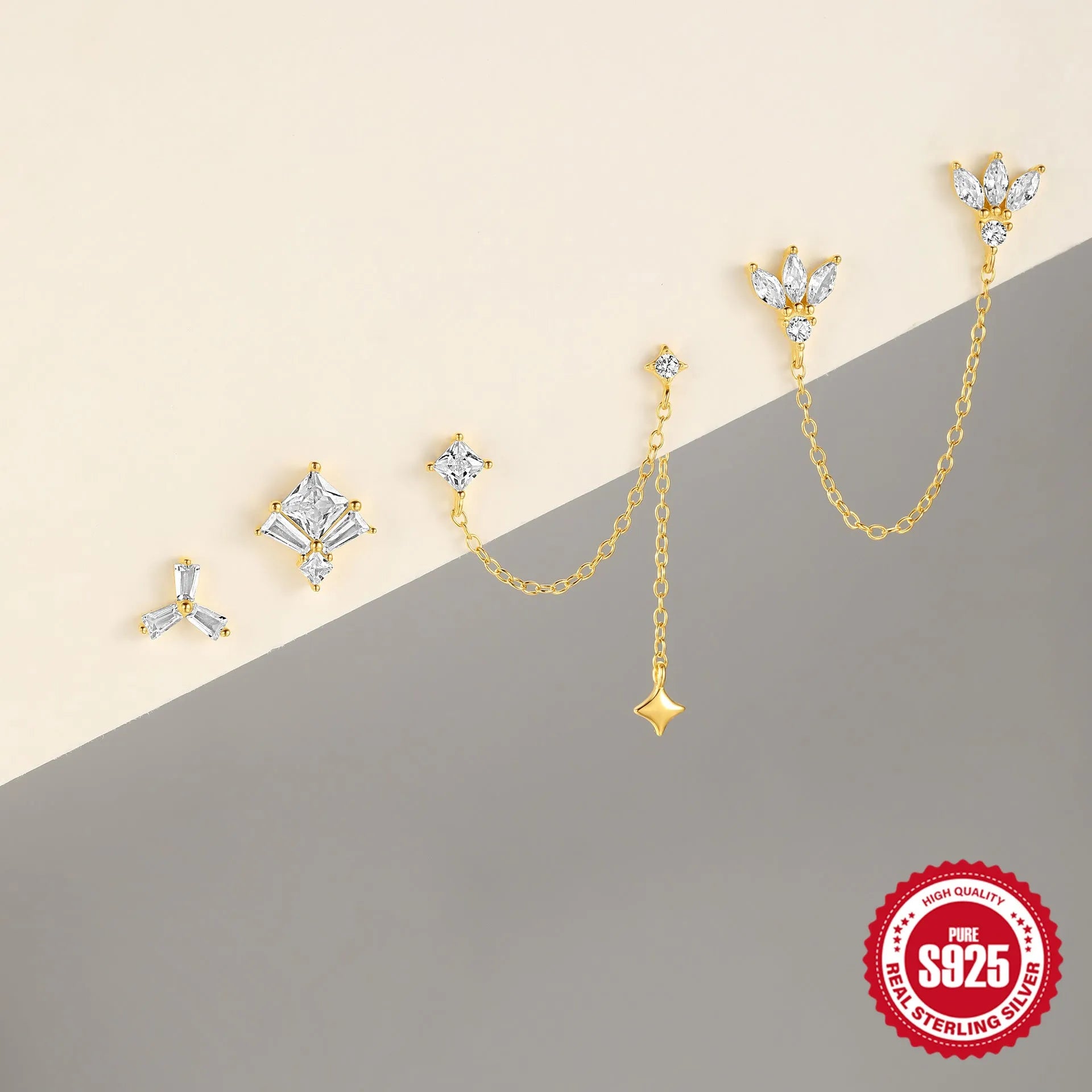 A pair of small golden-toned sterling silver stud earrings with inlaid zircon stones, featuring a delicate chain and clover design.